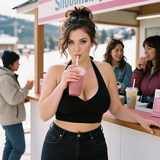 Photograph of a fair-skinned woman with black hair in a messy bun, sipping a pink smoothie at an outdoor café, wearing a black