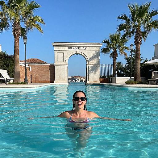 Photograph of a woman with dark hair and sunglasses in a blue swimming pool, with a 