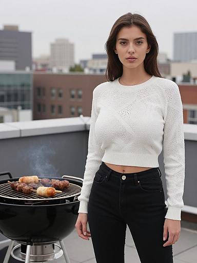 Photograph of a young woman with long brown hair, wearing a white knit sweater and black high-waisted jeans, standing on a rooftop grill with