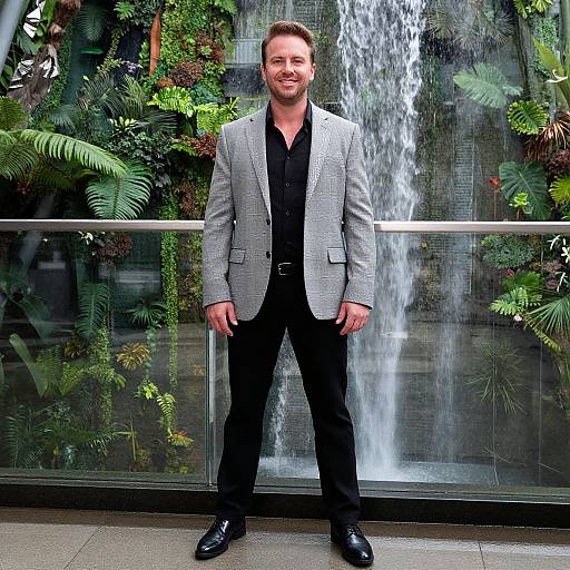 Smiling Man Standing by Waterfall and Greenery