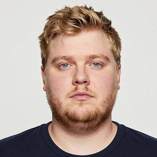 Photograph of a fair-skinned, bearded man with blue eyes, short messy blonde hair, wearing a black shirt, against a white background.