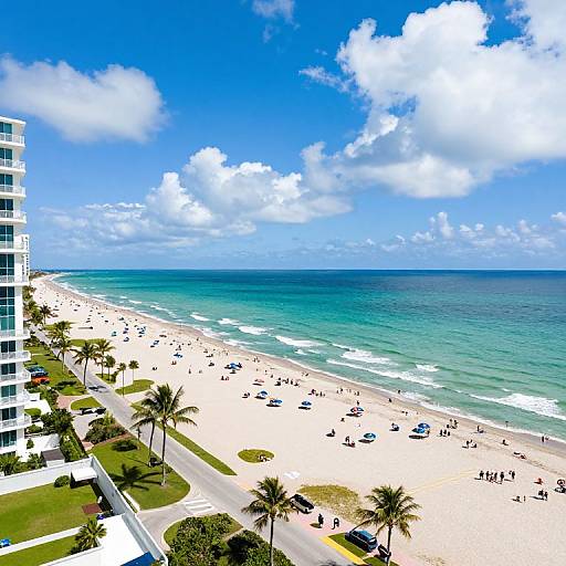 Photograph of a vibrant beach scene with clear turquoise water, white sandy shore, scattered beachgoers, palm trees, and a modern white building on