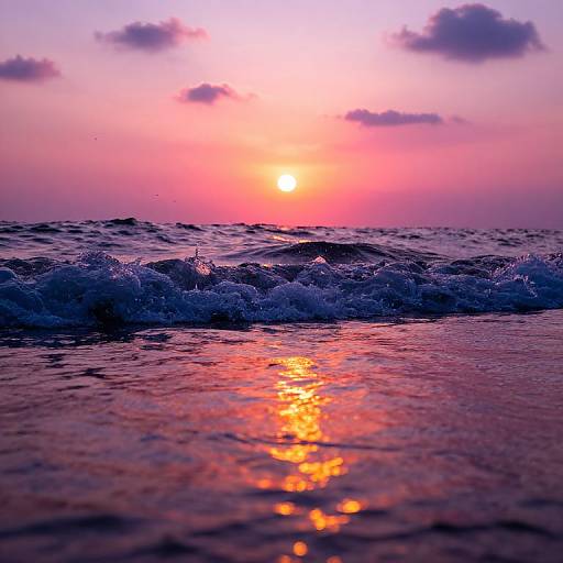 Photograph of a vibrant sunset over a calm ocean, with pink and purple hues in the sky, and orange reflections on the water, waves gently crashing
