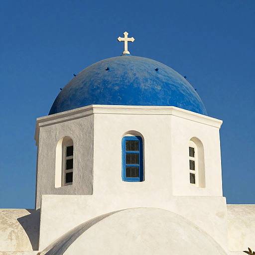 Photograph of a white Greek Orthodox church with a blue dome and white cross, set against a clear blue sky.