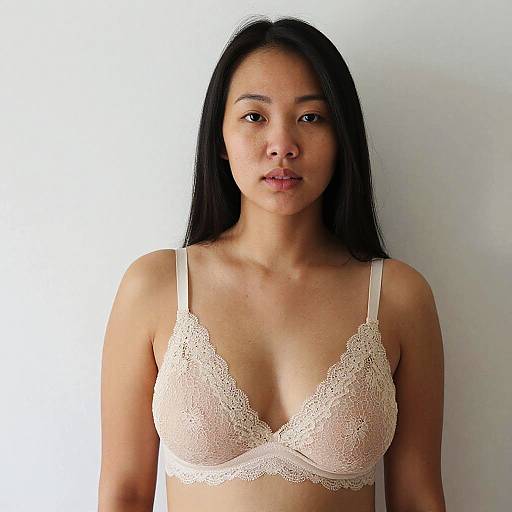 Photograph of an Asian woman with long black hair, wearing a white lace bra, standing against a plain white background.