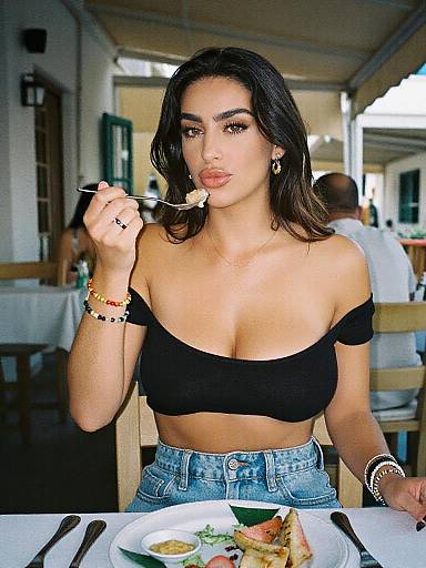 Photograph of a young woman with dark hair, tan skin, and medium breasts, wearing a black off-shoulder top and high-waisted