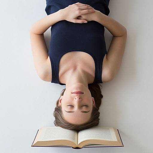 Photograph of a light-skinned woman with brown hair, lying on a white surface, eyes closed, wearing a black sleeveless top, hands on