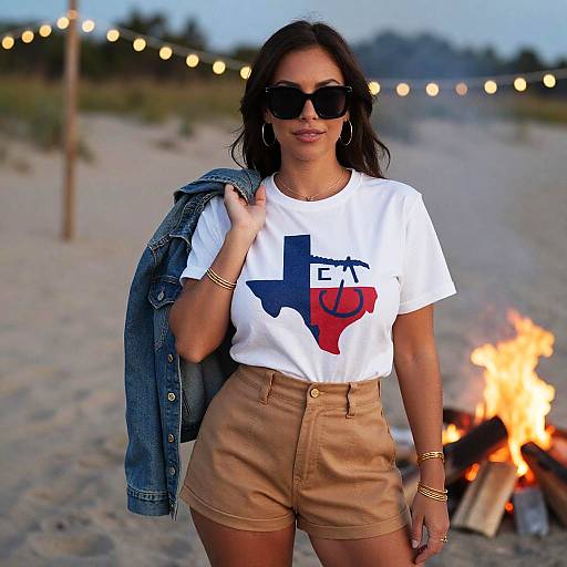 Photograph of a tan-skinned woman with long dark hair, wearing black sunglasses, white Texas-themed shirt, beige shorts, denim jacket, and gold