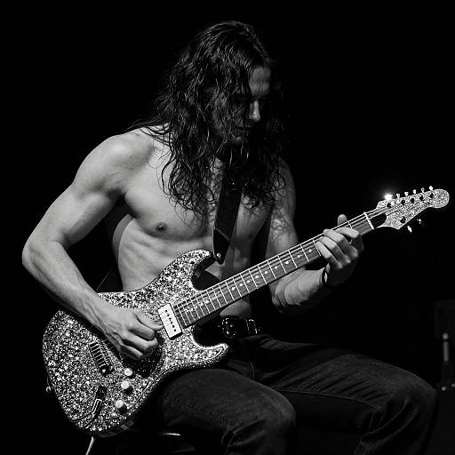 Photograph of a shirtless, muscular man with long, wet hair playing a glittery electric guitar against a black background. Intense, high-