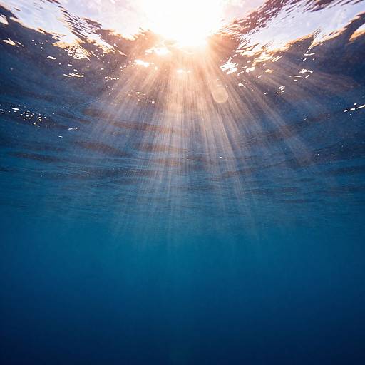 Photograph of sunlight penetrating deep blue underwater, rays of light streaming down through rippled water surface, creating a serene, ethereal effect.