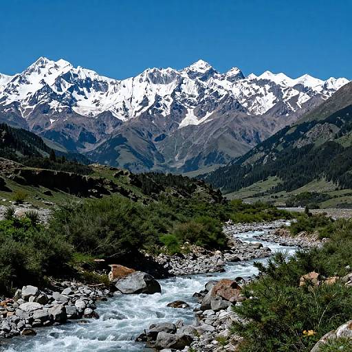 Photograph of a vibrant mountain landscape with snow-capped peaks under a clear blue sky, a rushing river flowing through rocky terrain, and green shrubs