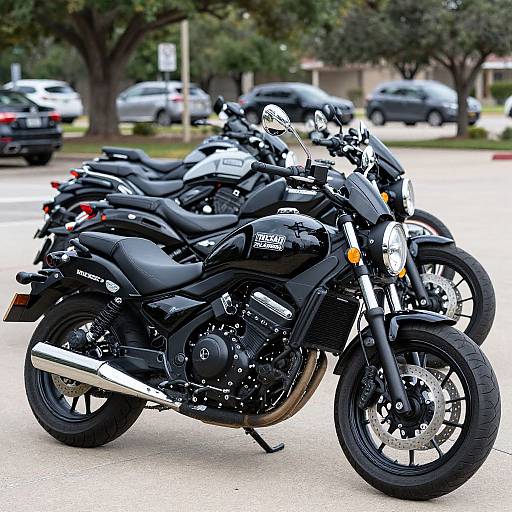 Photograph of five black motorcycles parked in a row on a suburban street, with blurred cars and trees in the background.
