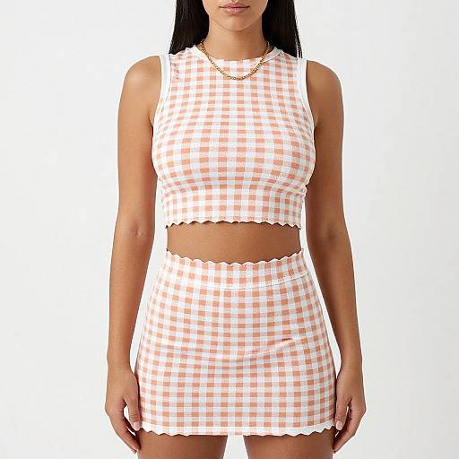 Photograph of a woman with long black hair wearing a sleeveless, white and orange gingham crop top and matching skirt, with scalloped edges
