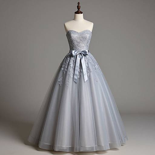 Photograph of a strapless, silver-gray, full-skirted ball gown with intricate lace embroidery, a sparkling bodice, and a satin bow