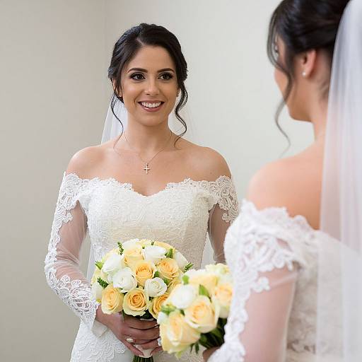 Photograph of a smiling bride in an off-the-shoulder lace wedding dress holding a bouquet of yellow and white roses, facing another bride in similar