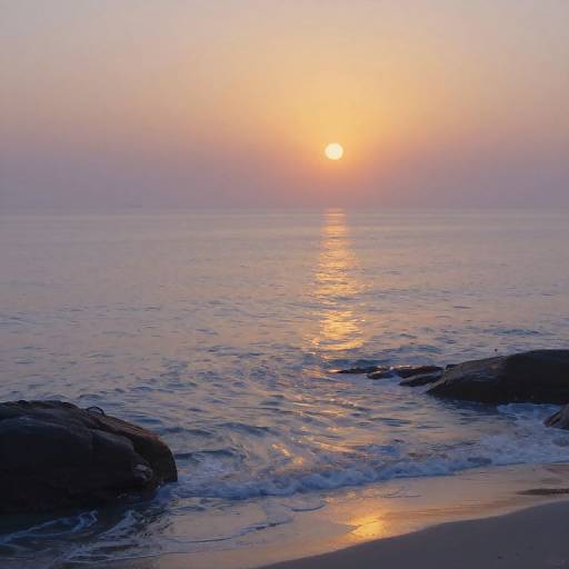 Photograph of a serene sunset over calm ocean waves, with the sun's golden reflection on the water and rocky shore in the foreground.