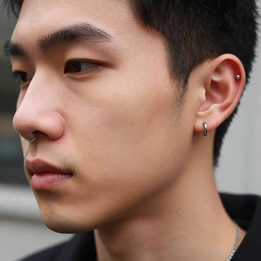 Close-up photograph of an Asian man with short black hair, wearing a nose ring, small hoop earring, and black shirt, looking to the left