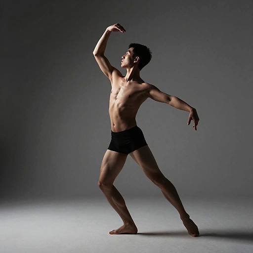Photograph of a muscular, shirtless male dancer in black briefs, striking a dynamic pose against a dark gray studio background.
