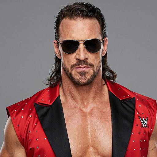 Photograph of a muscular man with long dark hair, beard, and sunglasses, wearing a red, black-trimmed, studded vest, exposing