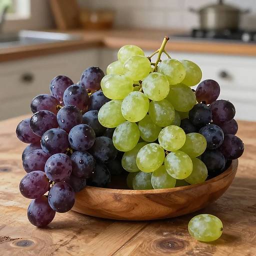 Photograph of a wooden bowl filled with vibrant green and deep purple grapes, placed on a rustic wooden table in a sunlit kitchen.