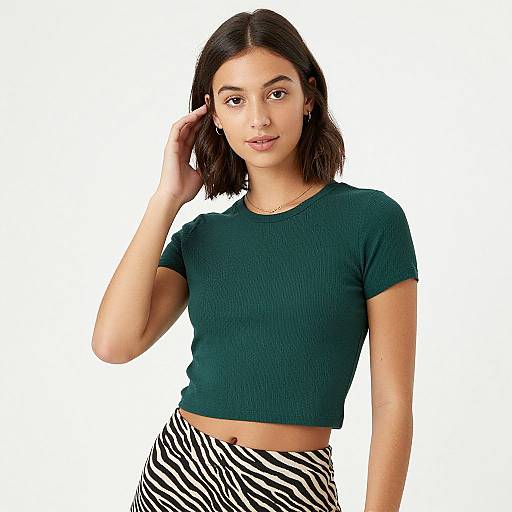 Photograph of a young woman with medium-length dark brown hair, wearing a green ribbed crop top and zebra-striped pants, standing against a white