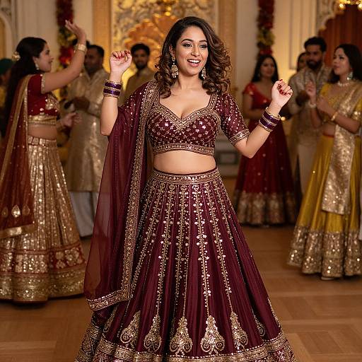 Photograph of a smiling South Asian woman in a maroon, gold-embellished traditional outfit, dancing with other women in similar attire in an