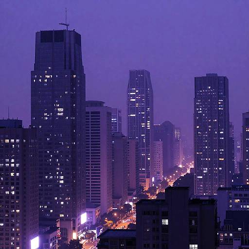 Photograph of a cityscape at dusk, featuring tall, illuminated skyscrapers with purple and blue hues, and a busy street below with glowing orange