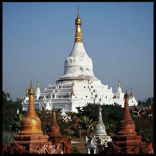 Photograph of a grand white Buddhist stupa with a golden spire, surrounded by smaller red-brick stupas and lush greenery, under a