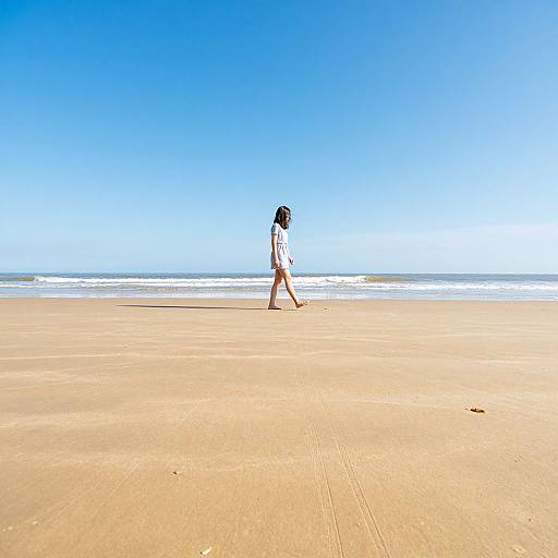 Photograph of a solitary woman with black hair, wearing a white top and brown shorts, walking on a vast, sandy beach under a clear, bright