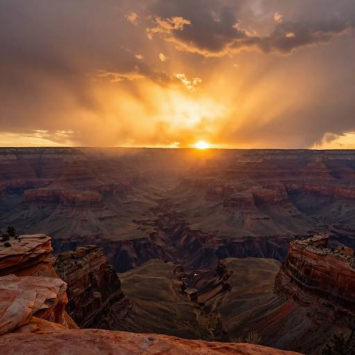 Photograph of a dramatic Grand Canyon sunset, featuring vibrant orange and yellow sky with sun rays, and deep, textured canyon shadows.