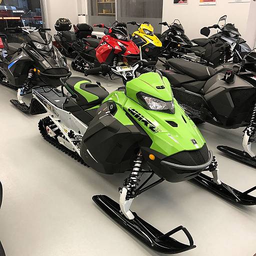 Photograph of a bright green snowmobile with black accents in a showroom, surrounded by various other snowmobiles in black, red, and yellow,