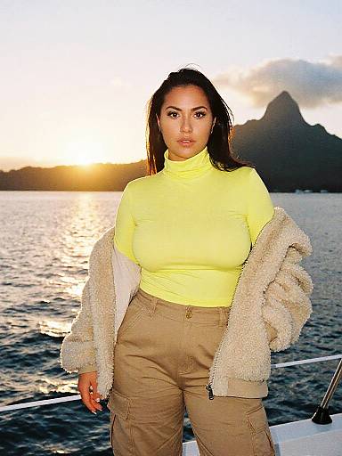 Photograph of a curvy woman with medium brown skin, long dark hair, wearing a yellow turtleneck, beige cargo pants, and a beige