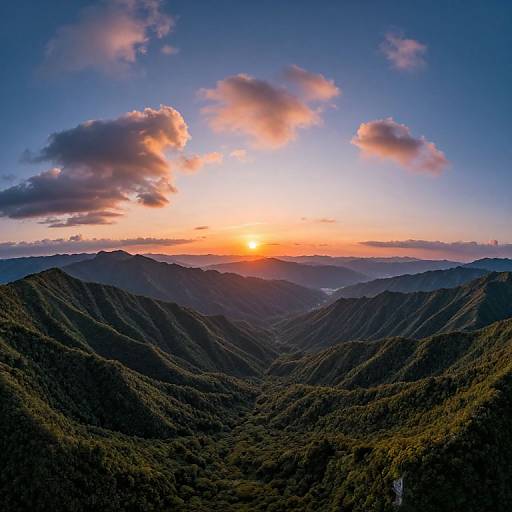 Photograph of a stunning mountain sunrise with vibrant orange and pink clouds above lush, dark green valleys and distant blue-hued peaks.
