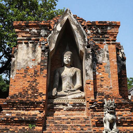 Photograph of a weathered, red-brick Buddhist temple with a serene, stone Buddha statue in the center and a small guardian statue at the bottom