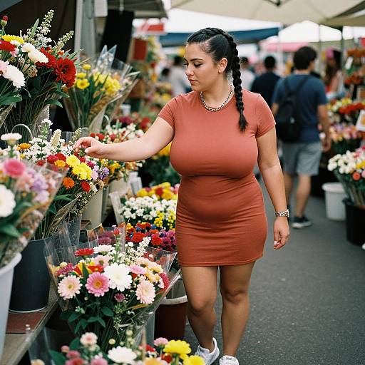 Photograph of a curvy Latina woman with long black braids, wearing a tight orange dress and white sneakers, browsing colorful flowers at an outdoor market