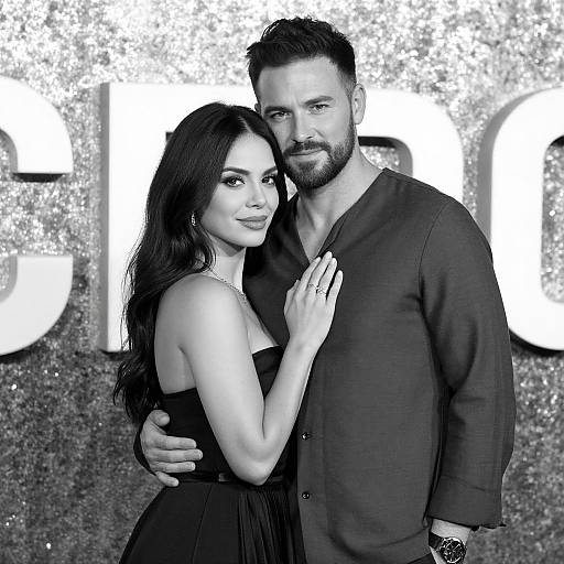 Black-and-white photograph of a bearded man in a dark shirt and a woman with long dark hair in a strapless dress, standing close, with