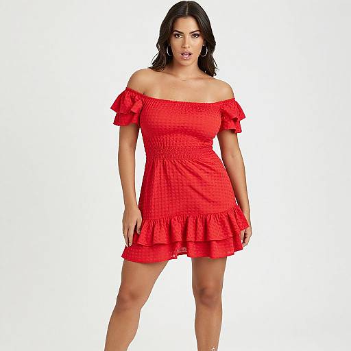 Photograph of a dark-haired woman with fair skin wearing a red off-shoulder, ruffled, short dress, standing against a plain white background