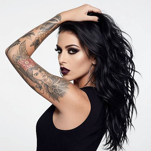 Photograph of a tattooed woman with black hair, dark lipstick, and a black sleeveless top, raising her arm against a white background.