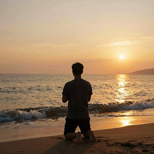 Photograph of a silhouette of a man in shorts kneeling on a beach at sunset, with golden sunlight reflecting on the ocean waves.