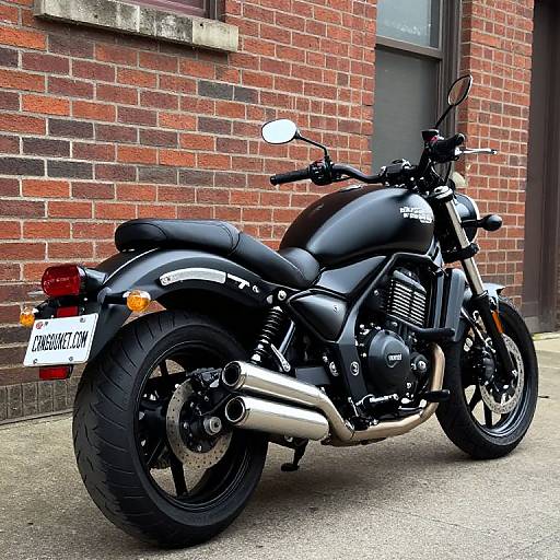Photograph of a black Triumph motorcycle with silver exhaust pipes, parked against a red brick wall, license plate 