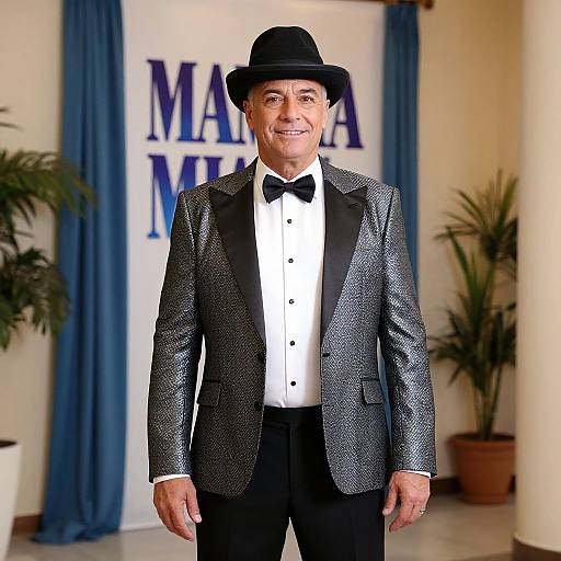 Photograph of an older man with light skin, wearing a black bowler hat, silver sequined tuxedo, black bow tie, white dress