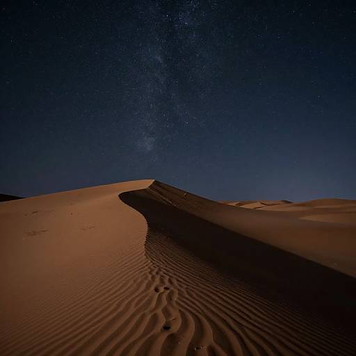 Photograph of a starry night sky over a desert with rippled sand dunes, illuminated by moonlight, creating a serene, cosmic landscape.