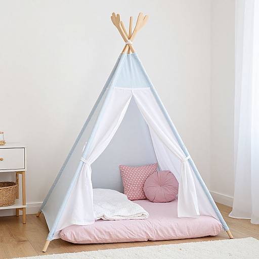 Photograph of a small, light-blue canvas teepee with white accents, pink bedding, and pink pillows, set in a bright, white-walled