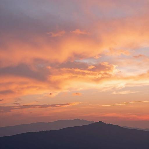 Photograph of a vibrant sunset sky with orange, pink, and purple clouds over a silhouette of distant mountain ranges.