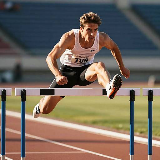 Athlete in mid-air, leaping over a hurdle on a sunlit track, wearing a white tank top and black shorts, with focused expression.