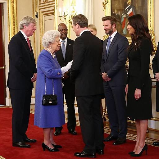 Photograph of Queen Elizabeth II in a blue coat and black handbag, shaking hands with six men and one woman in formal black attire, in an