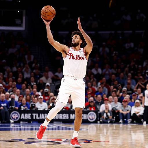 Photograph of a male basketball player in white Phoenix jersey, red shoes, and white shorts, mid-shot, holding the ball, with a blurred,