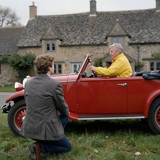 Man kneeling by vintage red car in rural village