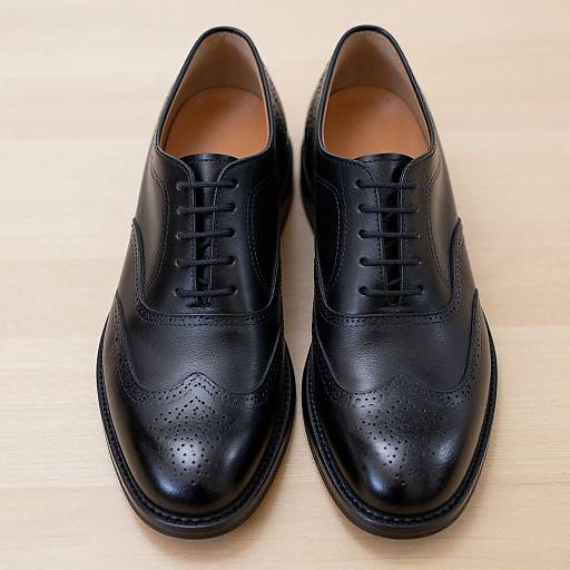 Photograph of a pair of polished black leather Derby shoes with lace-ups, placed side-by-side on a light wooden surface.