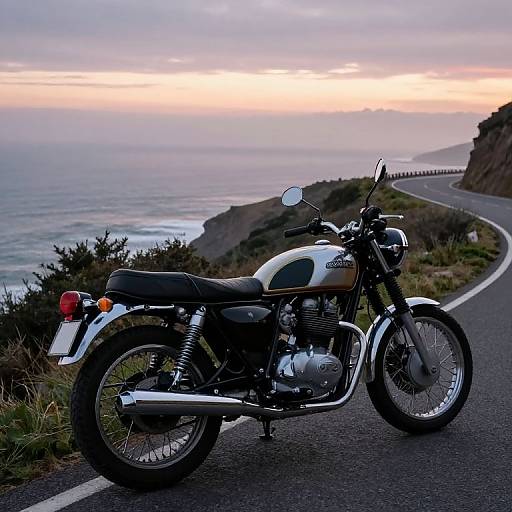 Photograph of a vintage white and green motorcycle parked on a coastal road at sunset, with ocean and cliffs in the background.